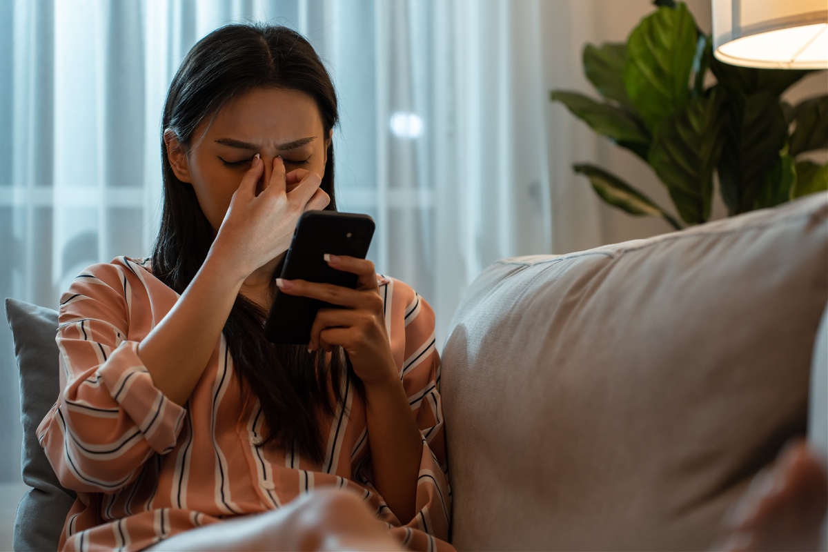 woman sitting on couch and holding the bridge of her nose in discomfort