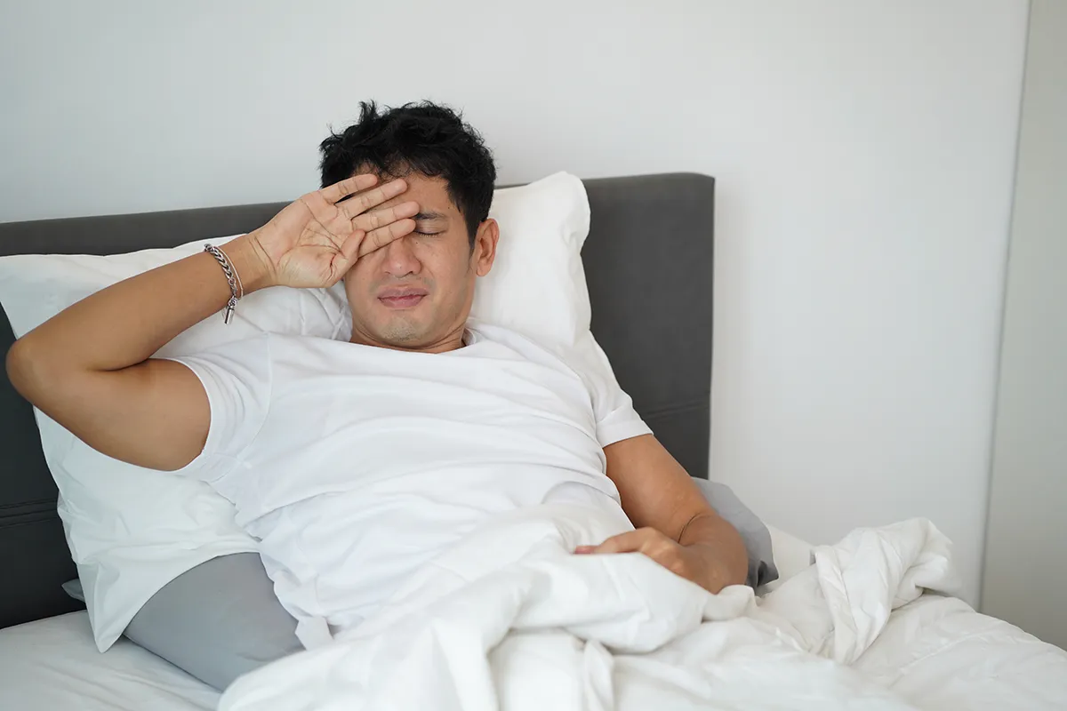 a man sitting in bed and rubbing his eye