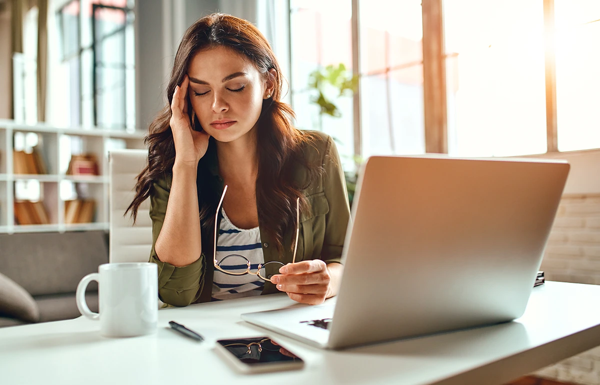 a woman sitting at her computer and holding a hand to her head