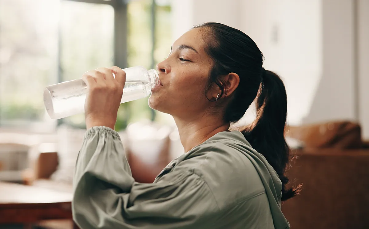 a woman drinking water from a bottle in her living room